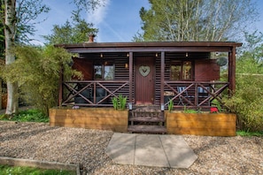 A wooden cabin with a porch, a heart-shaped decoration, and a gravel driveway.
