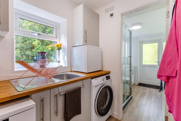 A compact kitchen with a washing machine, a sink, and a window with a view of greenery.