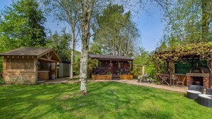 A wooden cabin with a patio, a barbecue area, and a pergola with vines.