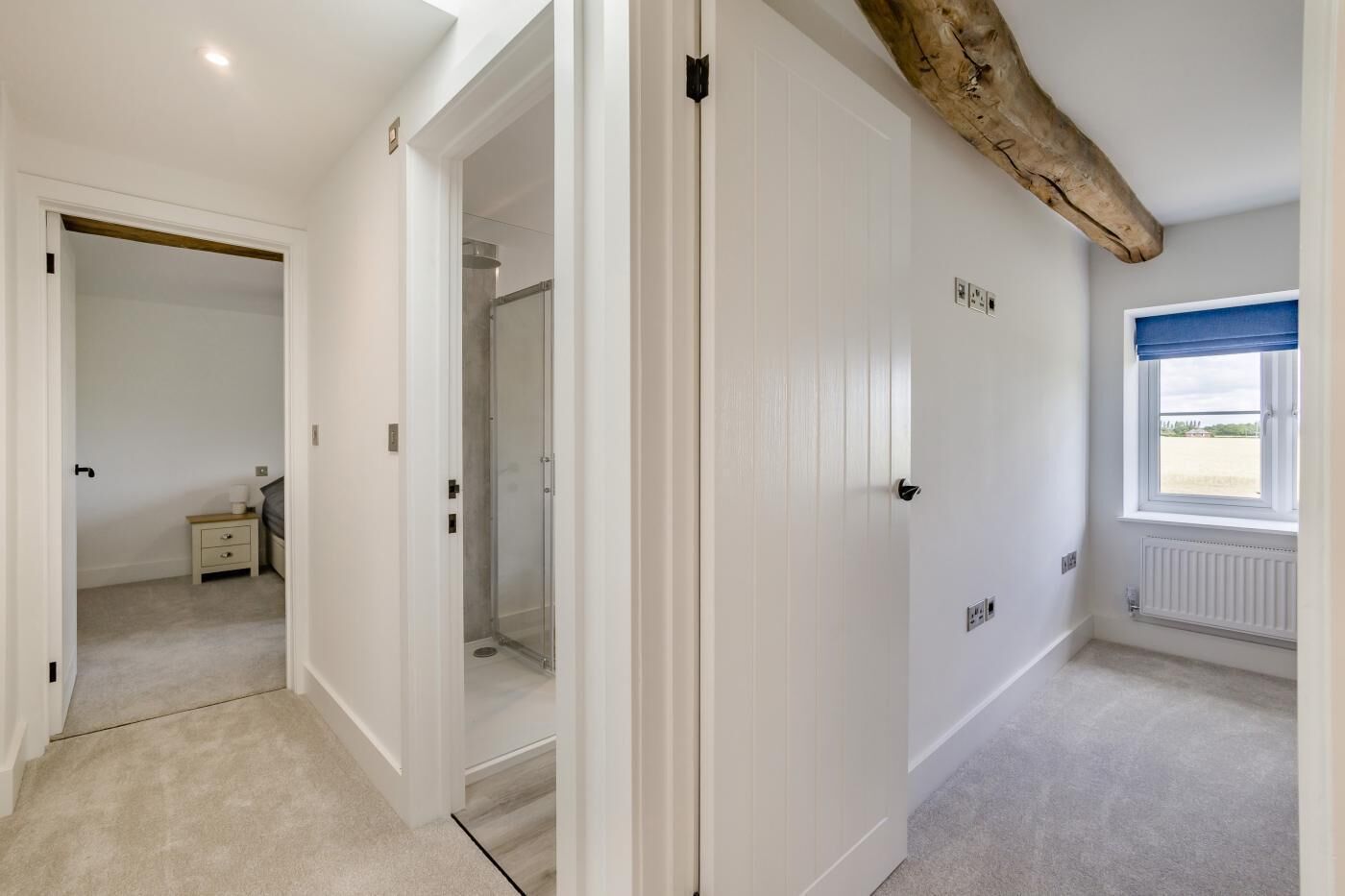 Una habitación con una viga de madera en el techo, una ventana con vistas y una puerta que da a otra estancia.