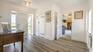 Un pasillo amplio con suelo de madera, paredes blancas y una puerta que da a una habitación con chimenea.