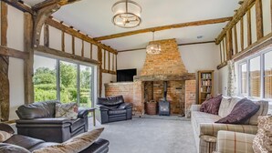 Una sala de estar acogedora con vigas de madera a la vista, chimenea de ladrillo, sofás de cuero y un ventanal con vistas a la vegetación.