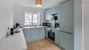 A modern kitchen with light blue cabinets, a stainless steel sink, a microwave, and an oven. - 3 Bed in Portreath (oc-c30852) (Portreath)