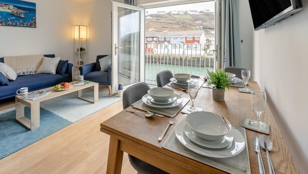 A modern living room with a sofa, coffee table, and dining area set up for a meal. - 3 Bed in Portreath (oc-c30852) (Portreath)
