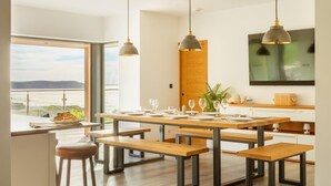 A modern kitchen with wooden tables and benches, pendant lighting, and a view of the sea. - 5 Bed in Mortehoe (oc-c30855) (Mortehoe)
