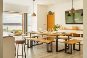 Une cuisine moderne avec des tables et des bancs en bois, des luminaires suspendus et une vue sur la mer.