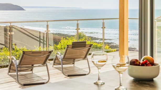 A balcony with two chairs and a table with a bowl of fruit and wine glasses. - 5 Bed in Mortehoe (oc-c30855) (Mortehoe)