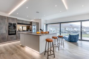 Une cuisine moderne dotée d’un îlot central, de tabourets de bar et offrant une vue sur un quartier résidentiel.
