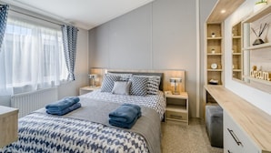 A modern bedroom with a large bed, bedside tables, a desk with shelves, and a window with curtains. - 2 Bed in Warton (oc-s31031) (Warton)