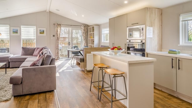 A modern kitchen with a central island, bar stools, and a dining area with a table and chairs. - 2 Bed in Warton (oc-s31031) (Warton)
