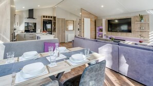 A modern kitchen with a built-in stove, a dining area with a table set for four, and a living area with a large flat-screen TV. - 2 Bed in Warton (oc-s31031) (Warton)