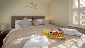 A neatly made bed with a tray of breakfast items, including croissants, grapes, and juice, in a well-lit room with a large window.