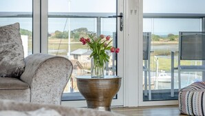 A modern living room with a large glass door leading to a balcony, a comfortable sofa, and a vase with flowers on a metal base. - 3 Bed in St. Helens (oc-y30961) (Saint Helens)
