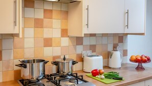 Una cuina amb dues olles d'acer inoxidable sobre una cuina de gas, una torradora blanca i un plat de fruita al taulell.