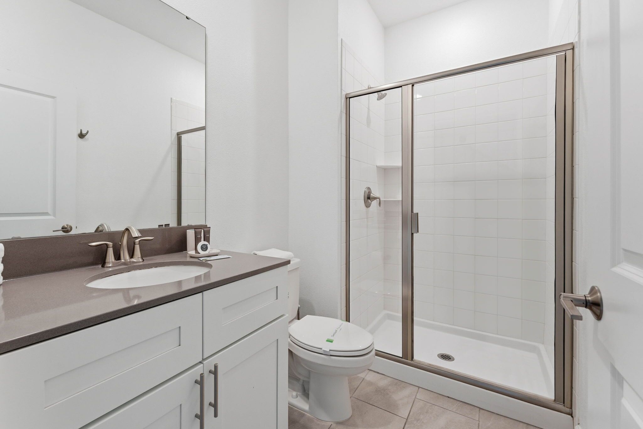 Ein modernes Badezimmer mit einer Duschkabine, einer weißen Toilette und einem Waschtisch mit Spiegel und Spüle.