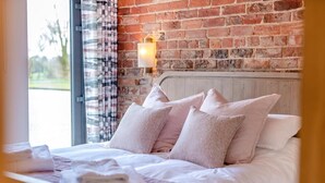 Ein Bett mit Kissen, ein Holzkopfende, eine Ziegelwand und ein Fenster mit Vorhängen.