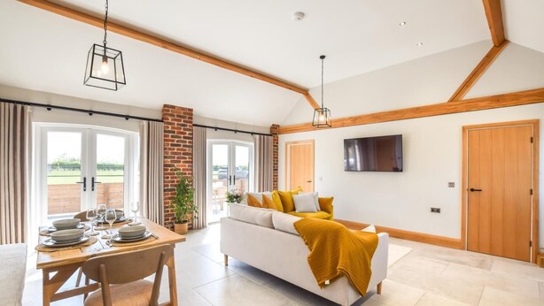 A modern living room with a sofa, a dining table set for two, and a TV mounted on the wall. - 2 Bed in Beeford (oc-t90892) (Beeford)