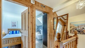 Een slaapkamer met houten vloer, een bed, een badkamer met bad en een trap met houten leuning.