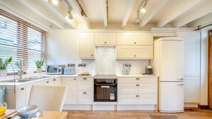 Een moderne keuken met witte kastjes, een magnetron, broodrooster en een koelkast. Er staat een eettafel met een stoel en een dienblad met croissants en sap.