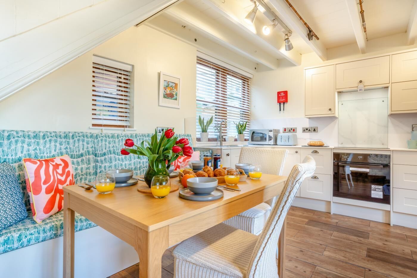 Una cucina moderna con zona pranzo, che presenta un tavolo in legno apparecchiato per la colazione, un divano con un cuscino colorato e vista sulla cucina dalla zona pranzo.