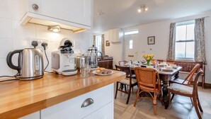 Et moderne køkken med træbordplade, rustfrie apparater og et spiseområde med fletstole og et bord dækket til to.