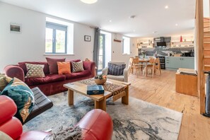 A modern living room with a red sofa, a wooden coffee table, and a dining area with a kitchen in the background. - 3 Bed in Milltown (oc-c30983) (Milltown)