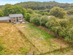 A stone building with a patio area, surrounded by a fenced yard with a variety of vegetation and a hilly landscape in the background. - 3 Bed in Milltown (oc-c30983) (Milltown)