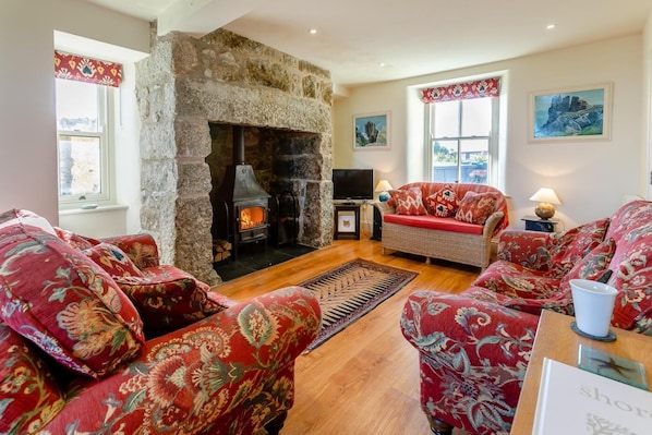 A cozy living room with a stone fireplace, patterned sofas, a television, and artwork on the walls.