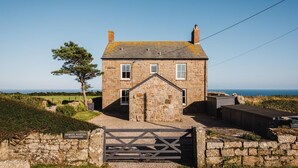 Une ferme en pierre avec une entrée fermée par un portail, un petit porche et une vue sur la mer.