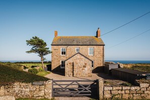 Une ferme en pierre avec une entrée fermée par un portail, un petit porche et une vue sur la mer.