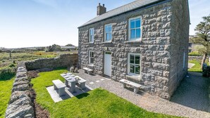 Une maison en pierre avec une cour verdoyante et un espace extérieur aménagé pour s’asseoir.