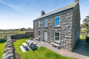 Une maison en pierre avec une cour verdoyante et un espace extérieur aménagé pour s’asseoir.