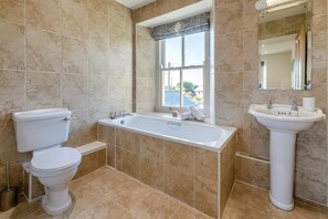 Une salle de bain comprenant des toilettes, une baignoire, un lavabo et une fenêtre.