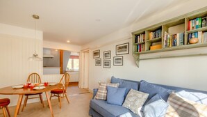 A cozy living room with a blue sofa, a wooden dining table, and a bookshelf filled with books. - 2 Bed in East Anstey (oc-k31022) (East Anstey)