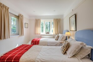 Une chambre avec deux lits, des rideaux beiges, une fenêtre donnant sur un paysage verdoyant, une lampe et un tableau encadré au mur.