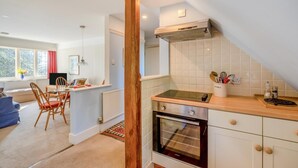 A compact kitchen with a built-in oven, a wooden column, and a dining area with a table and chairs. - 2 Bed in East Anstey (oc-k31022) (East Anstey)