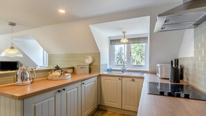 A modern kitchen with a wooden countertop, a built-in oven, a sink, and a window with a view of trees. - 1 Bed in East Anstey (oc-w31023) (East Anstey)