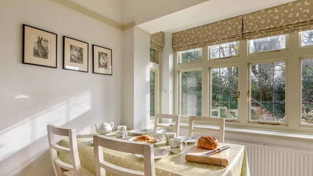 Uma área de refeições com uma mesa posta para dois, quadros nas paredes e vista para o verde lá fora.