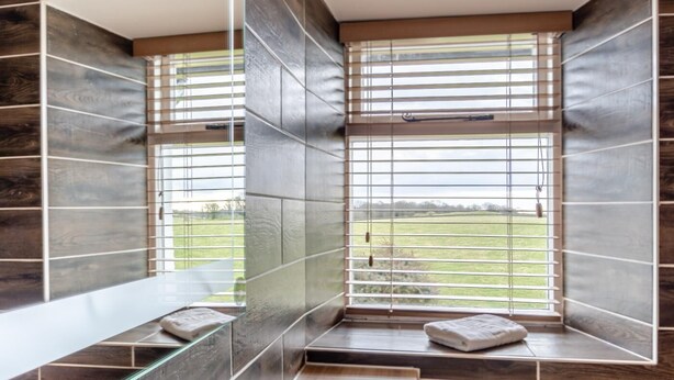 A bathroom with a large window, dark tiles, and a glass shelf. - 2 Bed in Field Broughton (oc-l31021) (Field Broughton)