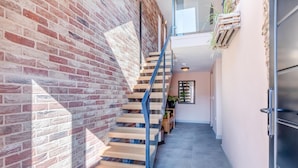 Una escalera moderna con escalones de madera y barandillas azules, que sube a un segundo piso con vista al cielo.