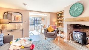 Una sala de estar acogedora con chimenea, comedor con mobiliario exterior y un reloj grande de color verde en la pared.