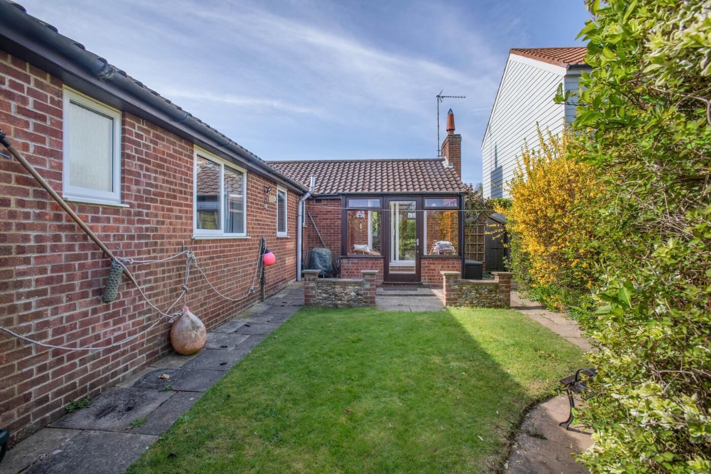 A brick house with a tiled roof, a glass conservatory, and a well-maintained lawn.