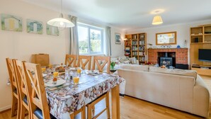A cozy living room with a fireplace, a dining area with a table set for breakfast, and a bookshelf filled with books. - 3 Bed in Brancaster (oc-r30695) (Brancaster)
