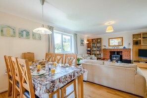 Ein gemütliches Wohnzimmer mit Kamin, einem Essbereich mit gedecktem Tisch für das Frühstück und einem Bücherregal voller Bücher.