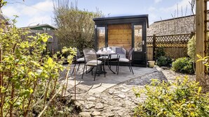 Un patio con mesa y sillas, una estructura de madera y un sendero de piedra.