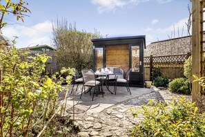 Eine Terrasse mit Tisch und Stühlen, einer Holzkonstruktion und einem gepflasterten Weg.