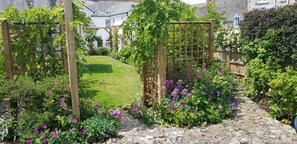 Ein Garten mit Holzranken, einem Kiesweg und verschiedenen blühenden Pflanzen.