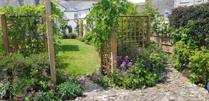 A garden with a wooden trellis, a stone pathway, and various flowering plants. - 2 Bed in Burton Bradstock (oc-h30904) (Burton Bradstock)