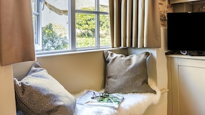 Una habitación con ventana, televisor y un banco acolchado con almohadones.