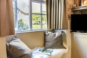 Ein Zimmer mit Fenster, Fernseher und gepolstertem Sitzplatz mit Kissen.